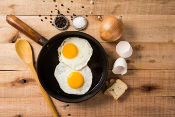 fried eggs, in a frying pan, on wooden background. Top wiew.