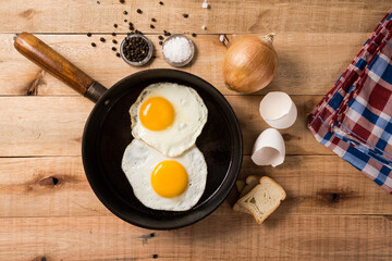 fried eggs, in a frying pan, on wooden background. Top wiew.