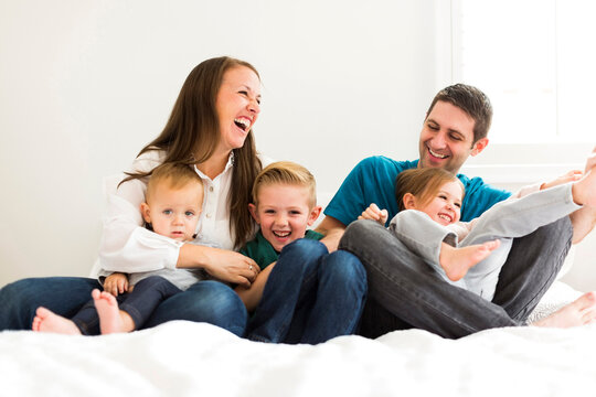 Family with three children (2-3, 4-5) laughing on bed