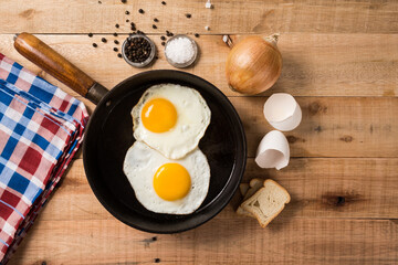 fried eggs, in a frying pan, on wooden background. Top wiew.
