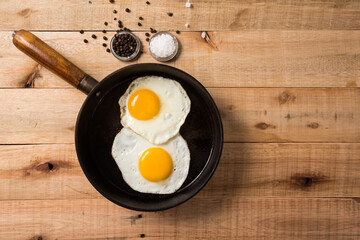 fried eggs, in a frying pan, on wooden background. Top wiew.