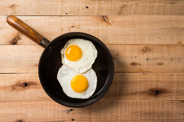 fried eggs, in a frying pan, on wooden background. Top wiew.