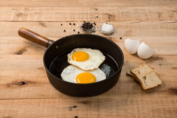 fried eggs, in a frying pan, on wooden background.