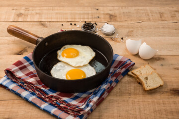 fried eggs, in a frying pan, on wooden background.