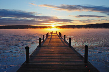 Symmetrical view of jetty on frozen lake, hills in background at sunrise