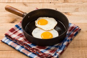 fried eggs, in a frying pan, on wooden background.