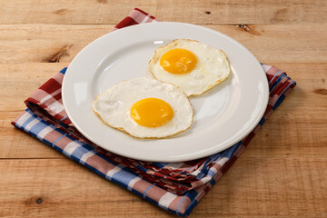 fried eggs, on a white plate, on wooden background.
