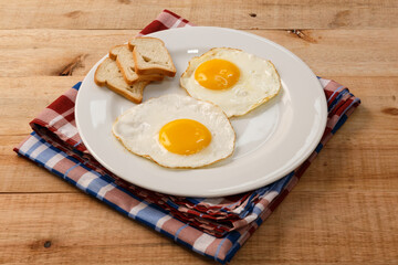 fried eggs, on a white plate, on wooden background.