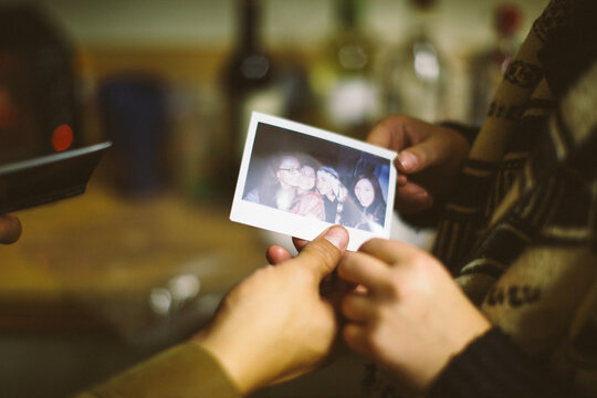 Two friends pass a polaroid photograph between themselves.