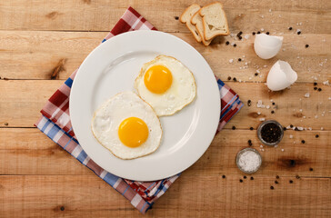 fried eggs, on a white plate, on wooden background. Top Wiew