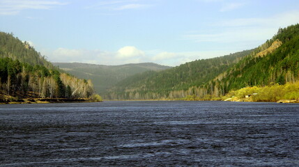 A wide river runs slowly towards the wooded mountains.