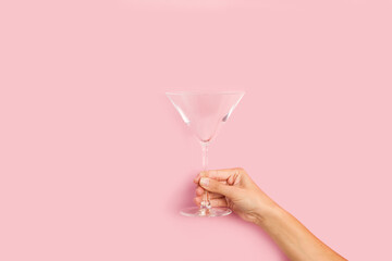 Mano de mujer elegante sosteniendo una copa de cristal sobre un fondo rosa pastel liso y aislado. Vista de frente. Copy space - obrazy, fototapety, plakaty