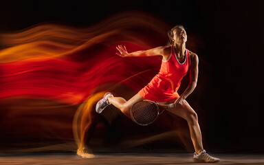 Champion. Professional female tennis player training isolated on black studio background in mixed light. Woman in sportsuit practicing. Healthy lifestyle, sport, workout, motion and action concept.