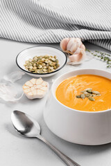 A bowl of pumpkin cream kabocha soup, garnished with pumpkin seeds, served with cream. Close-up, gray concrete background. Healthly food