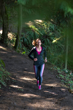Mature woman running on a sun speckled trail.