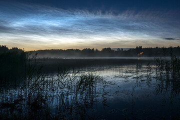 night landscape with white silver clouds over the lake, blurred foreground, charming cloud reflections in the lake water, summer night