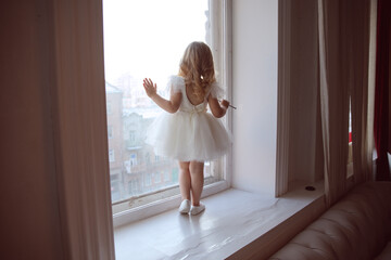 back of the dress with an open back. a little girl in a smart, fluffy white dress  near the window...