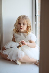 a little girl in a smart, fluffy white dress with a magic wand in her hands near the window and waits for Santa Claus or the tooth fairy. children's fairy tales and dreams. new year holiday.