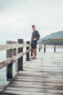 Portrait image of young man on wooden boardwalk by sea looking off frame