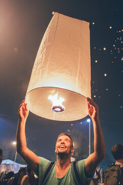 Festival time - Young man smiling and making a wish while releasing a fire lantern into the sky