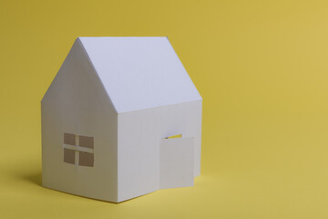White family paper house in man hand on yellow background paper. Minimalistic style. Copy space. View from above. Vertical orientation.