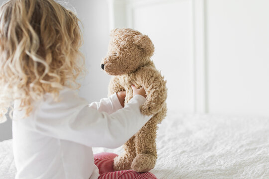 Young girl wearing red and white striped pajamas holding teddy bear up