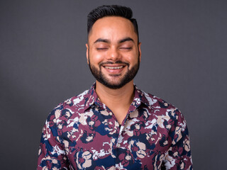 Young bearded Indian man against gray background
