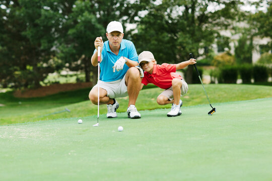 father teaching his son how to line up a putt - Powered by Adobe