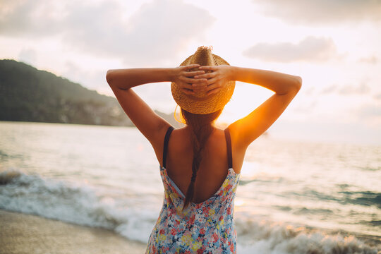 Young woman with hat watching sunset on the beach.