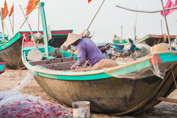 Fototapeta na wymiar Fishermen repairing nets on a boat trip out to sea in the afternoon July 31, 2014 at the beach of Hai Ly, Vietnam.