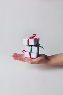 Hand holding a stack of small white Christmas boxes tied with ribbon