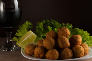 Salt cod fritters in a white plate with fresh lemons,salad and wine cup. Selective focus. Copy space