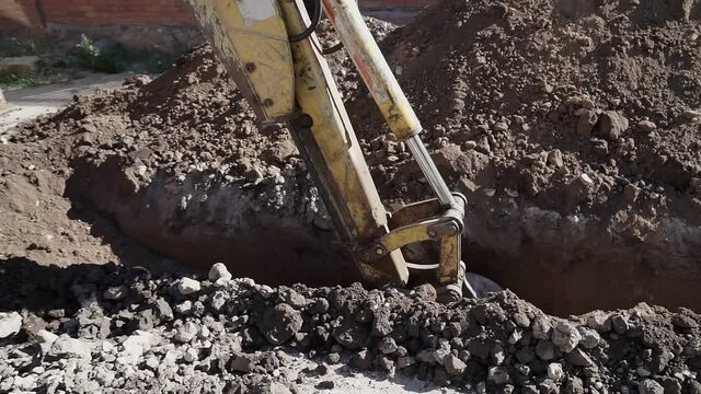 Big metal excavator bucket scoops up dirt while digging a ditch during roadworks in countryside. Ripper bucket excavating soil and rocks at a construction site on a sunny day.