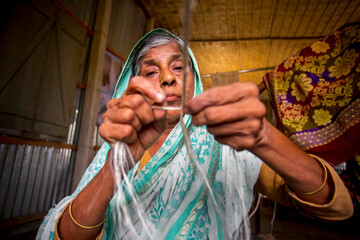 Fototapeta premium An old age woman is making on his skinny hands a rope from the banana tree fiber at Madhupur, Tangail, Bangladesh.