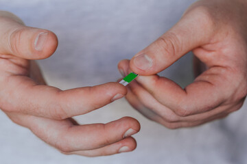 diabetes, healthcare - close up of a man with a glucometer and a test strip checking blood sugar at home