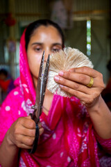 Naklejka premium A woman making handicrafts is smoothing the fibers of a banana tree with scissors in Madhupur, Tangail, Bangladesh.