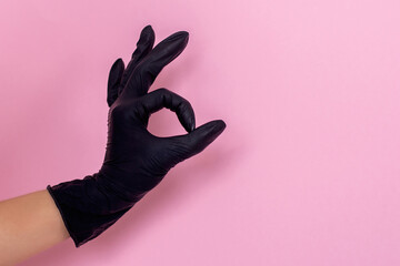 Female hand in black gloves making OK sign on pink background. Safety measures.