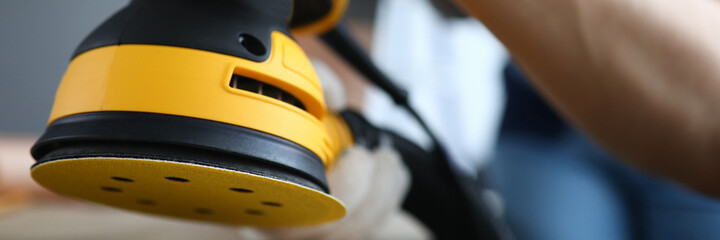 Close-up of persons hands polishing ground with grinding machine. Bright yellow sander instrument and craftsman on construction site. Protective gloves for work. Renovation concept