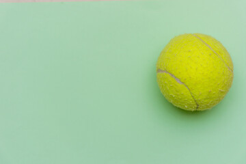 Bright yellow tennis ball on a solid pastel green flat lay background symbolizing sports and activity with copy space.