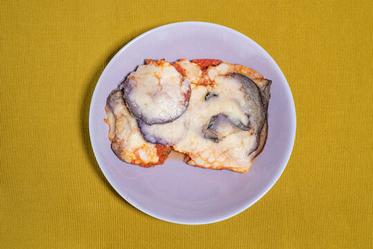 Aubergine Parmigiana Served In A Lilac Colored Dish Placed On A Light Green Table Runner