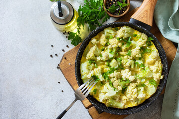 Healthy breakfast or diet lunch. Egg omelet with cauliflower in a cast-iron pan on a light stone table top. Flat lay top view. Copy space.