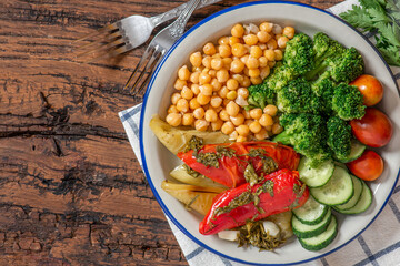 Cooked chickpeas with vegetables. Boiled chickpeas with broccoli, baked peppers, tomatoes and cucumbers in a plate on a wooden background top view. Vegetarian and vegan food.