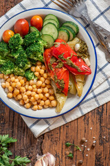 Cooked chickpeas with vegetables. Boiled chickpeas with broccoli, baked peppers, tomatoes and cucumbers in a plate on a wooden background top view. Vegetarian and vegan food.