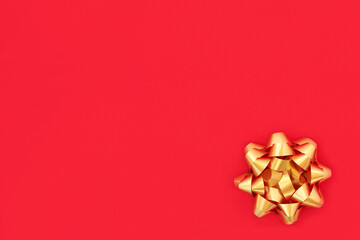 Christmas gold ribbon bow on red wrapping paper background. Minimal design symbol for the festive Xmas season, birthdays & Valentines.