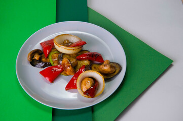 Side view of vegetarian dish. Mix of Grilled vegetables on gray plate. Colorful green background. Grilled mushrooms, bell pepper, onion, zucchini and eggplant served with fresh dill. Healthy food 
