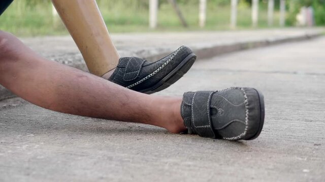 Slow motion of a poor disabled man  wearing a left prosthetic leg and a disabled left arm is sitting on the sidewalk on the roadside.