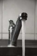 Clean water flows from the white metal faucet in the kitchen, close-up, selective focus.