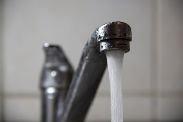 Clean water flows from the white metal faucet in the kitchen, close-up, selective focus.