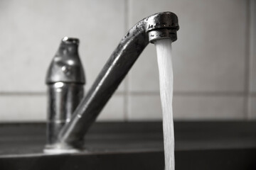 Clean water flows from the white metal faucet in the kitchen, close-up, selective focus.