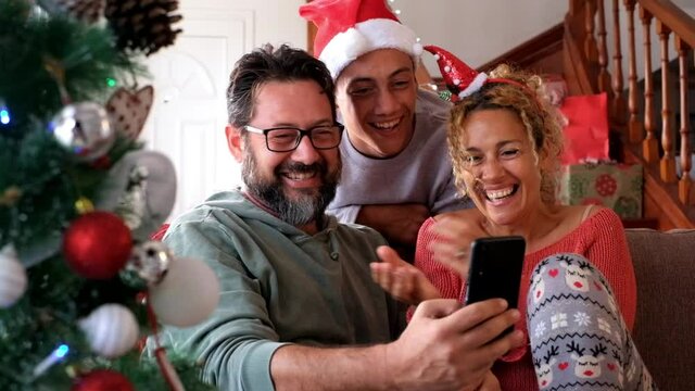 Happy caucasian family at home celebrating together Christmas Eve day with joy and love - concept of video call conference with friends and parents with internet connection - mother father and son